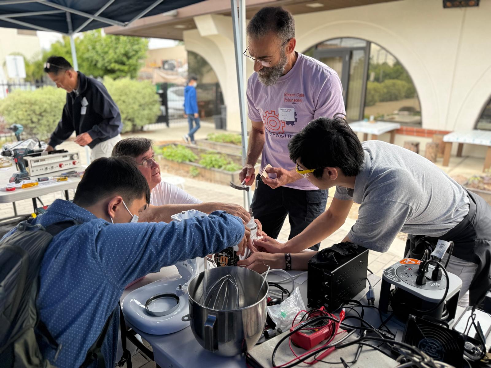 Volunteers at a repair café working together to fix a stand mixer on a workbench